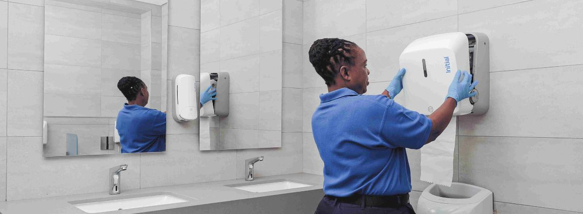 A female technician installing a modern silver hand dryer on a bathroom wall.